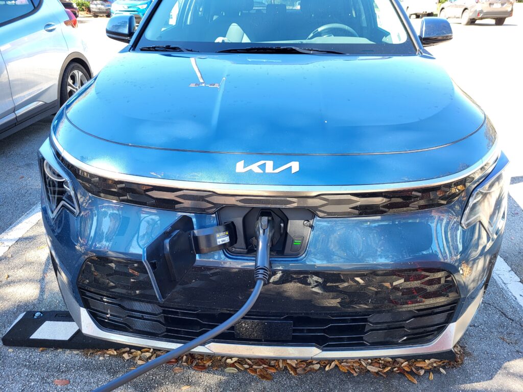 A blue Kia Niro electric car plugged in to a car charger. 