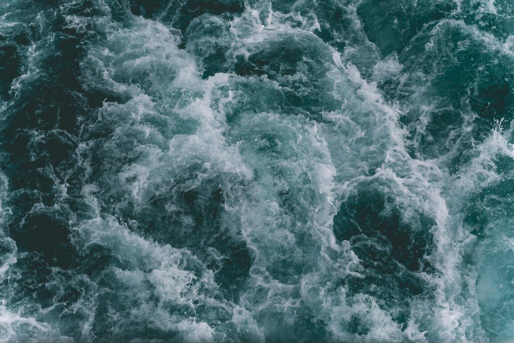 Multiple white-capped, frothy waves in a dark ocean.