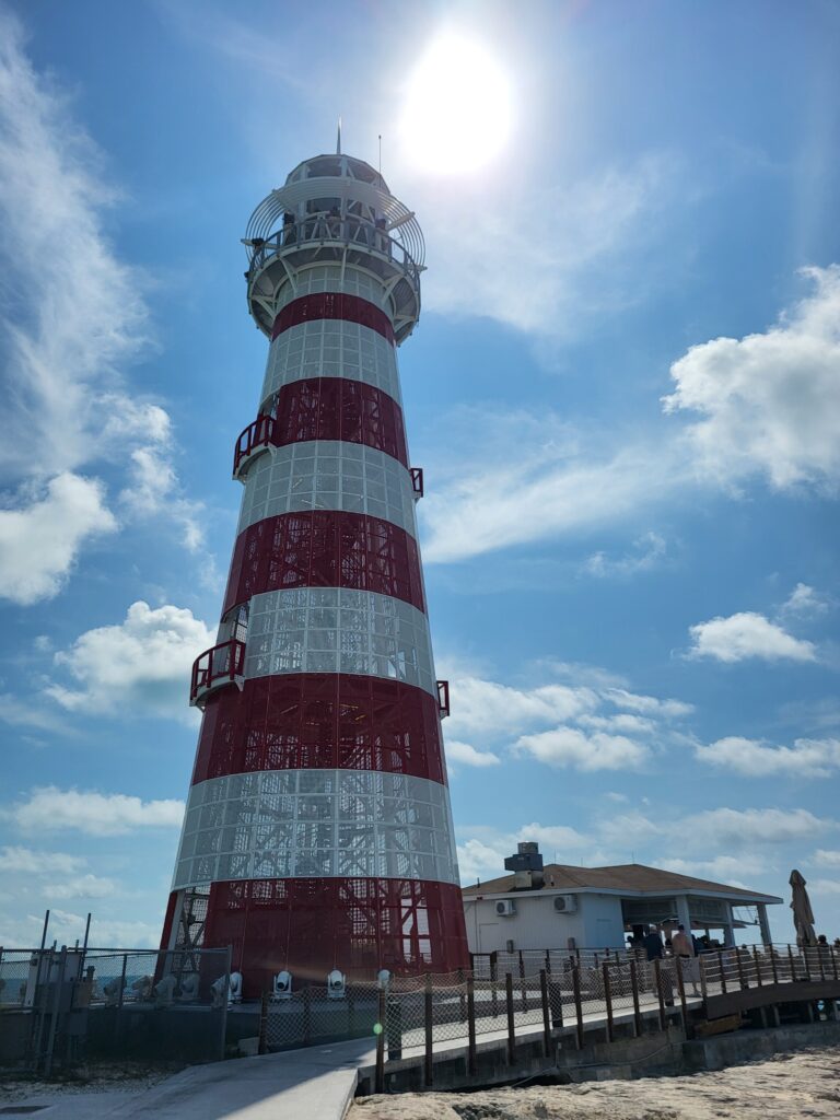 A red and white striped lighthouse near a beach bar.