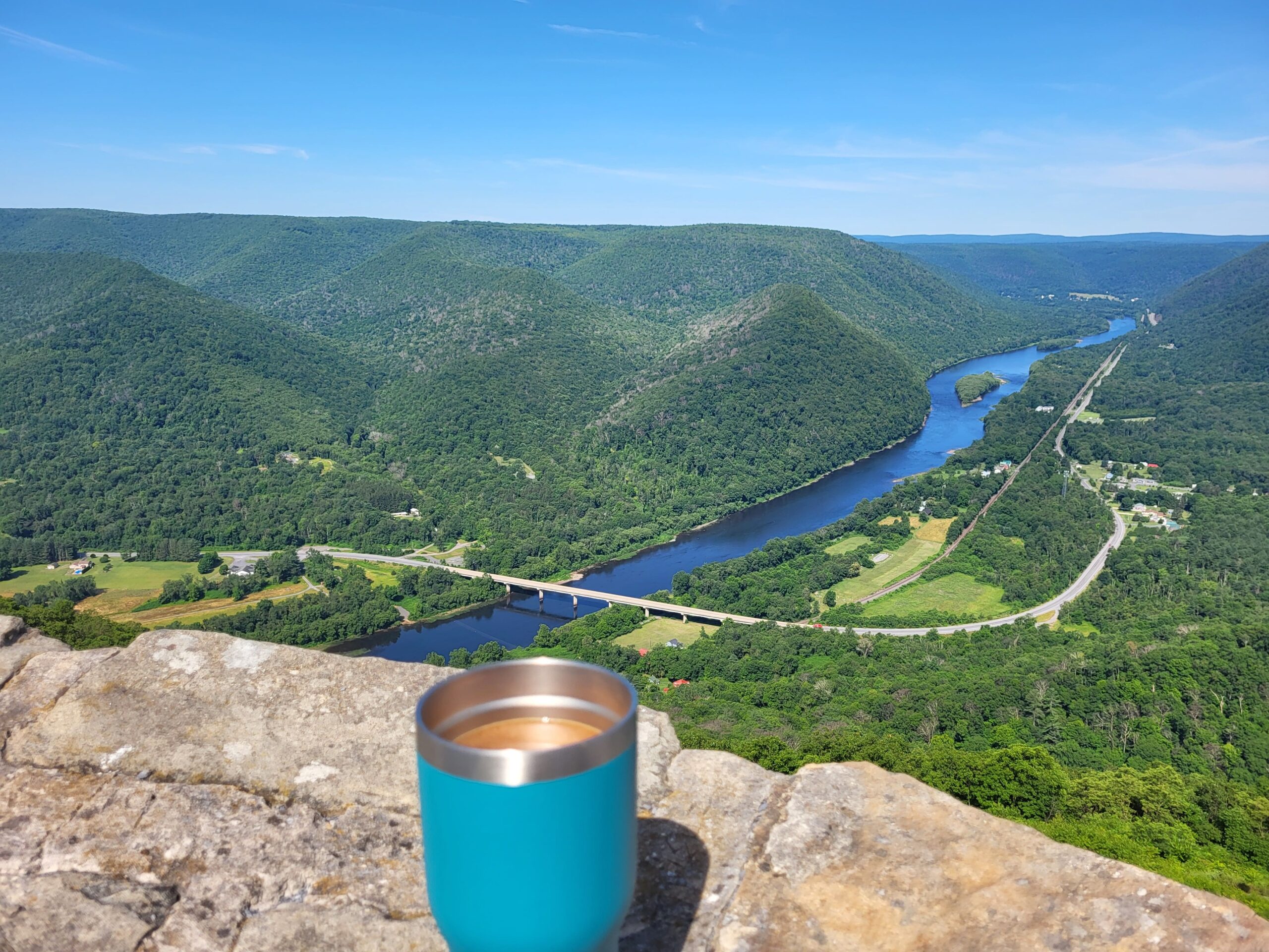 Coffee in a blue mug sitting on the rim of the overlook of the West Branch Susquehanna River